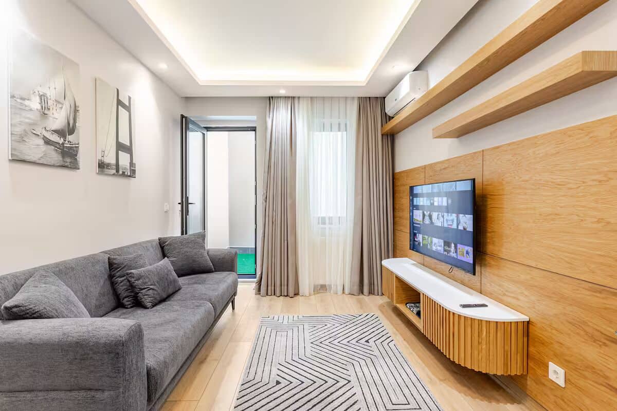A modern living room with a grey sofa, a wooden entertainment unit, and a large flat-screen TV.
