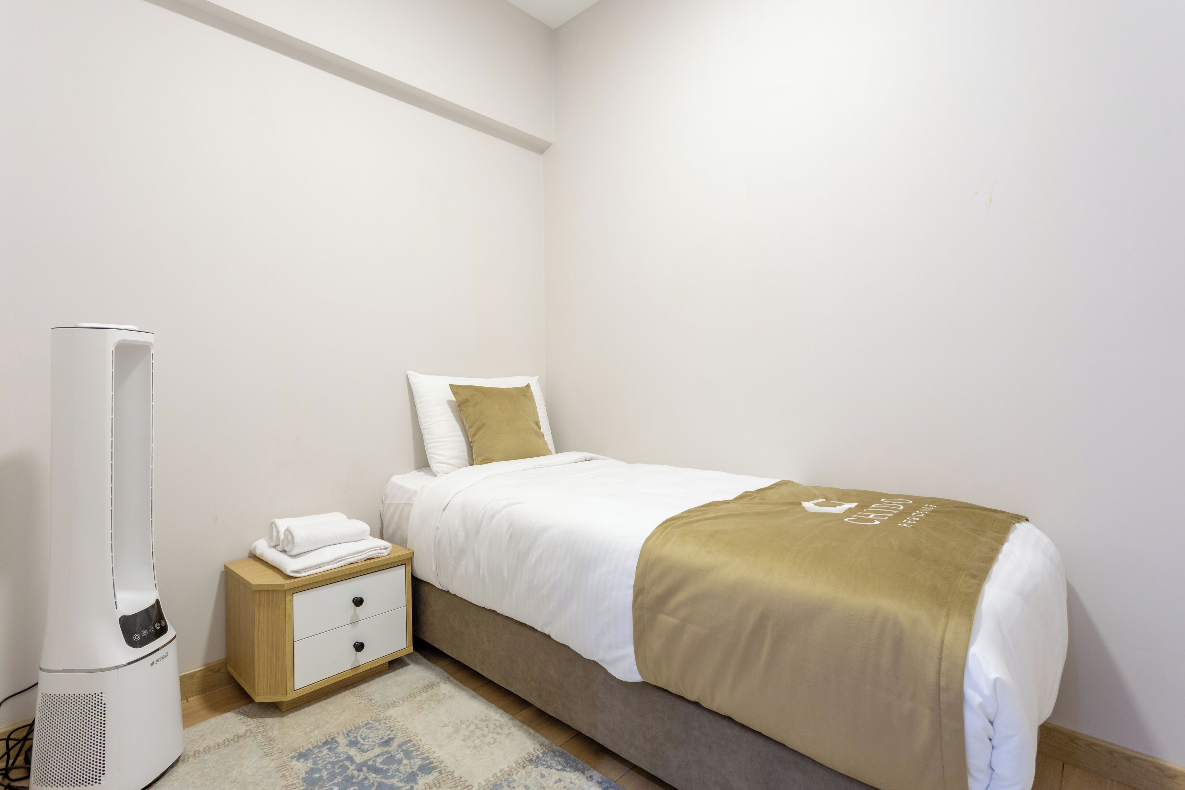 A neatly arranged bedroom with a bed, bedside table, and a portable heater.