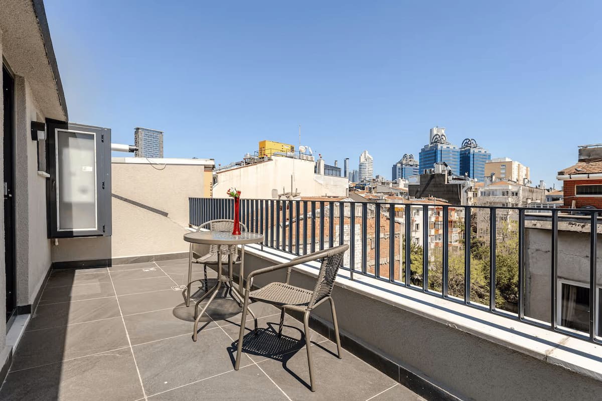 A balcony with a table and chairs, a vase with flowers, and a cityscape view.