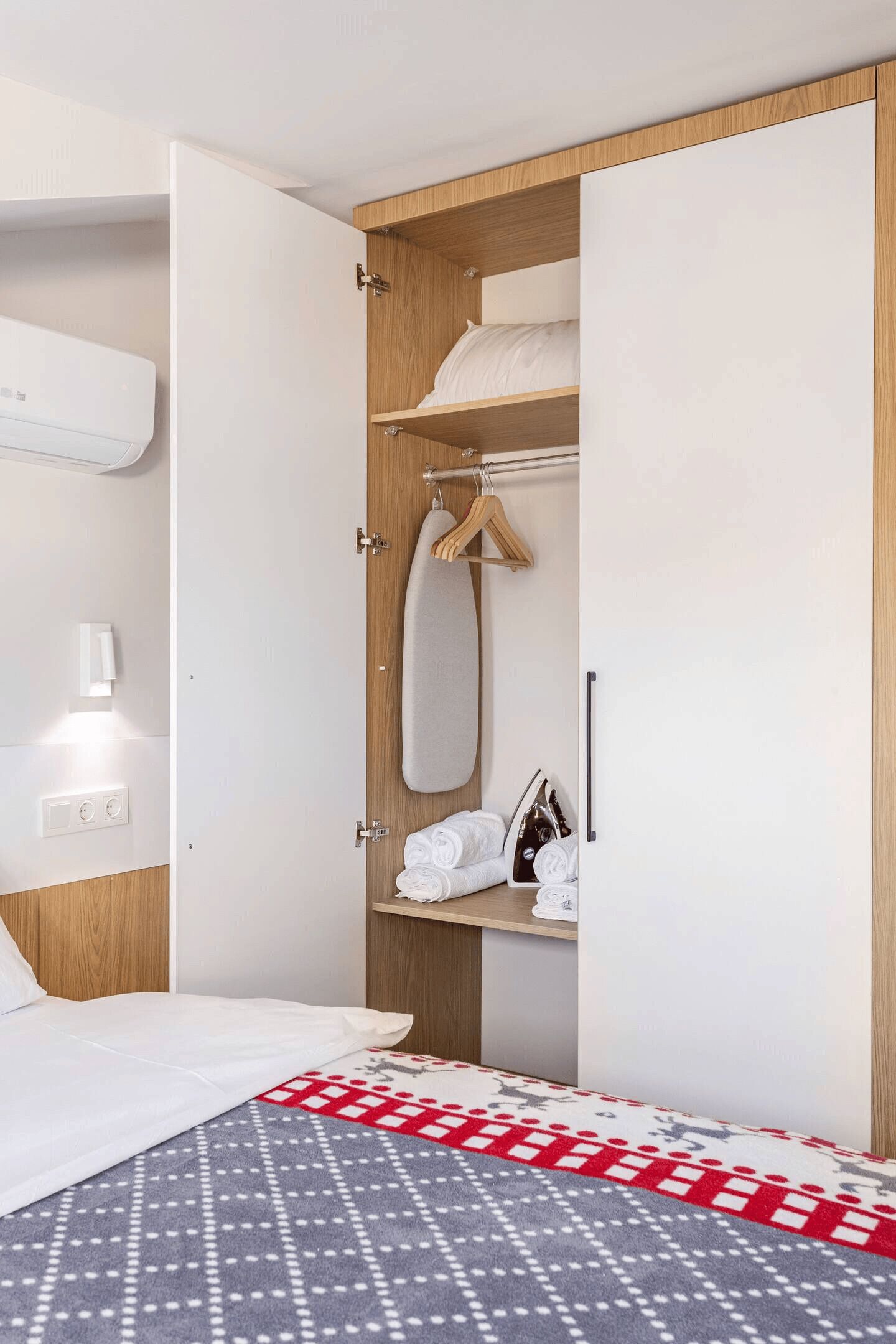 A hotel room with a bed, a wardrobe with hanging clothes, and a towel rack.