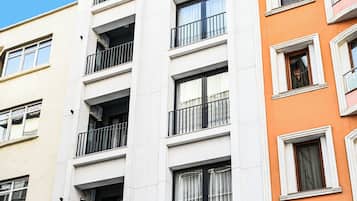 Un edificio de varios pisos con balcones, una entrada visible con un letrero y un automóvil estacionado adelante.