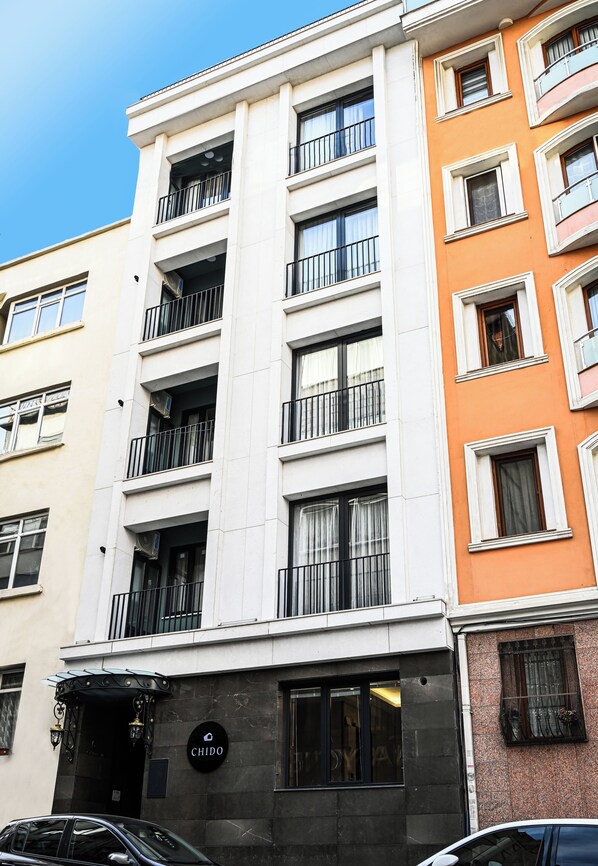 A multi-story building with balconies, a visible entrance with a sign, and a car parked in front. - Chido Residence (Istanbul)