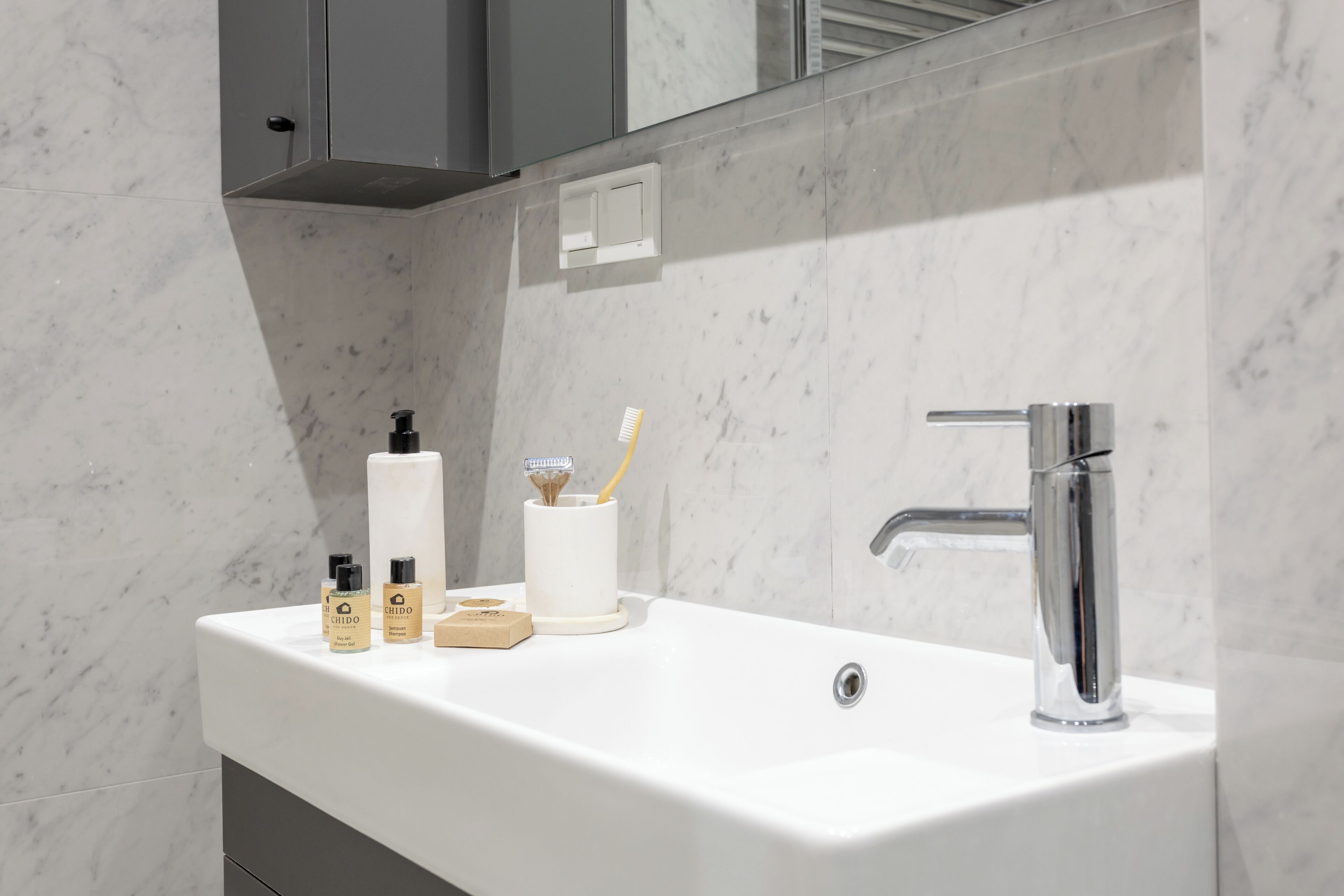 A bathroom with a white sink, a mirror, and toiletries.