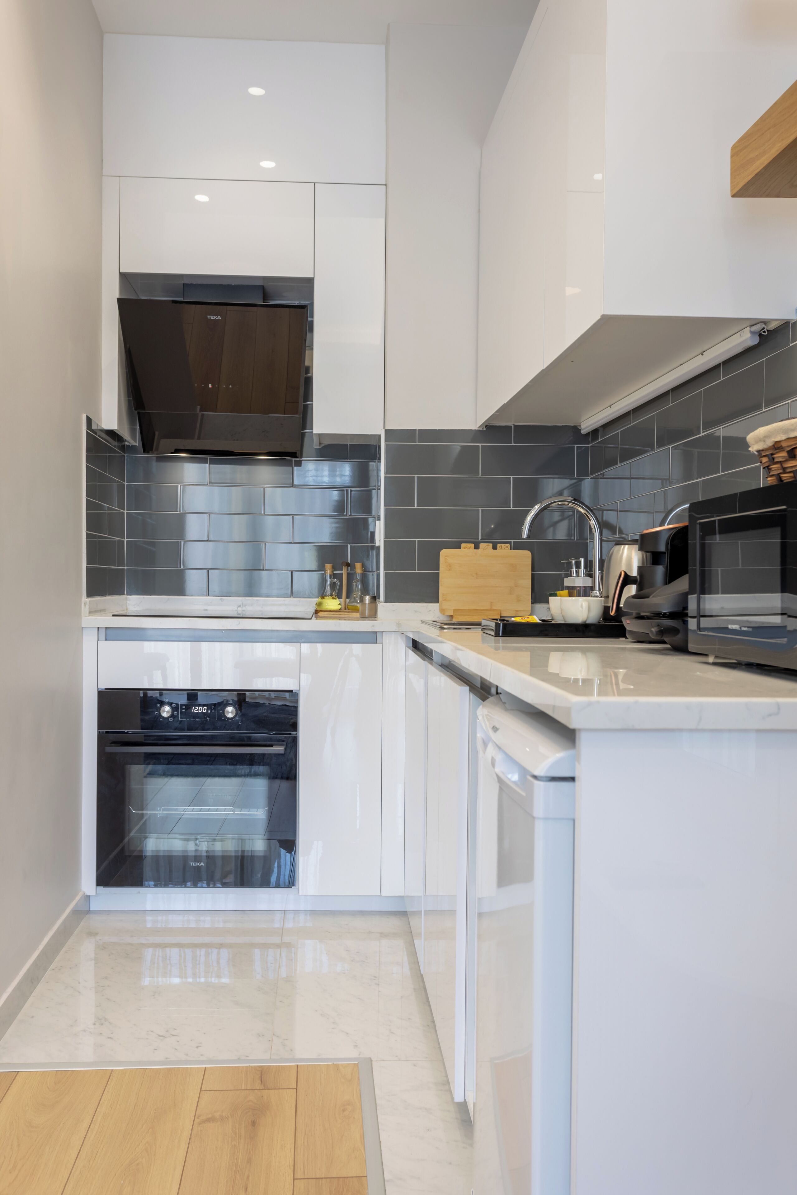 A modern kitchen with white cabinetry, a stainless steel range hood, and a built-in oven.