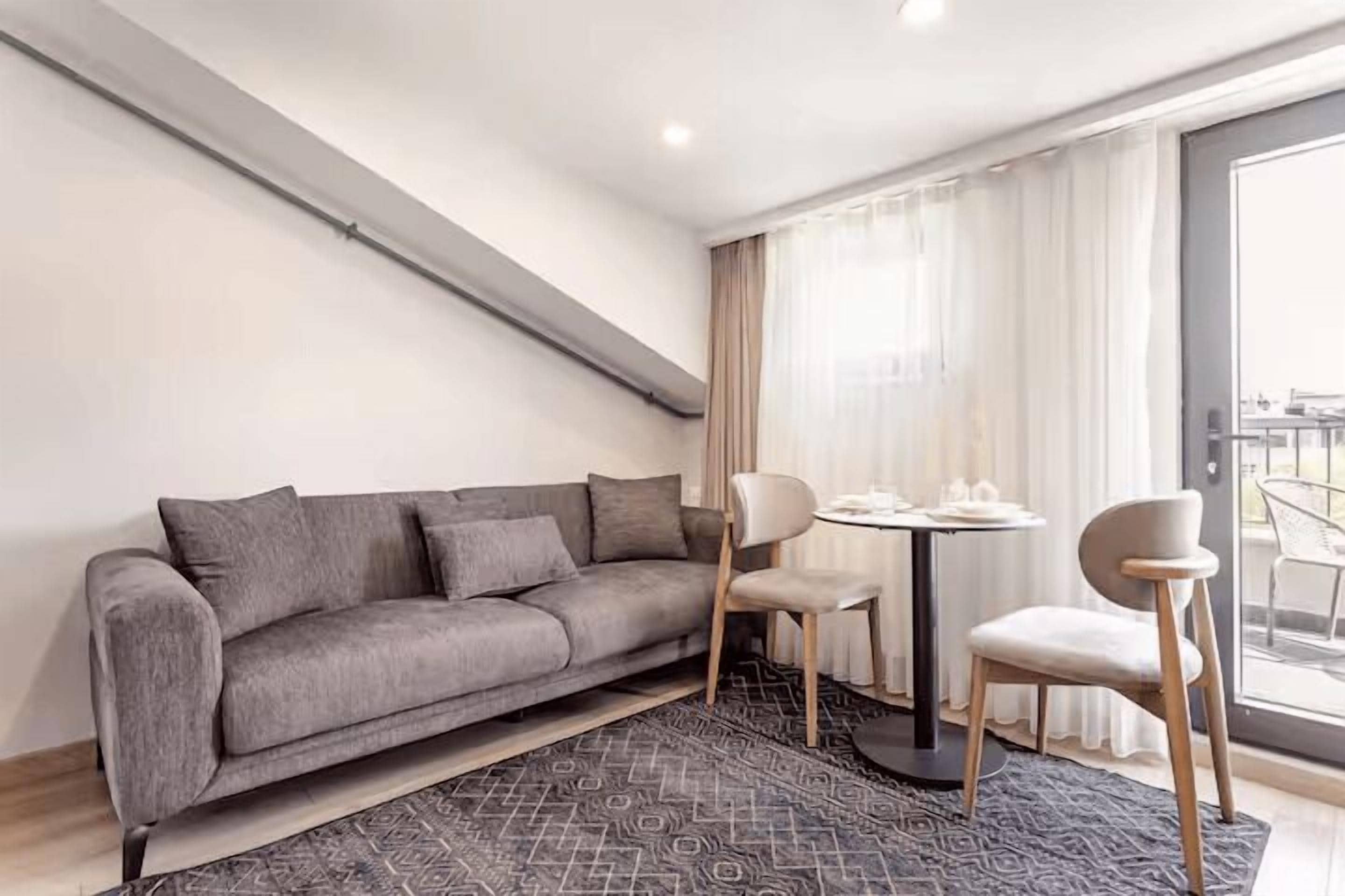 A modern living room with a grey sofa, two chairs, a small round table, and a patterned rug.