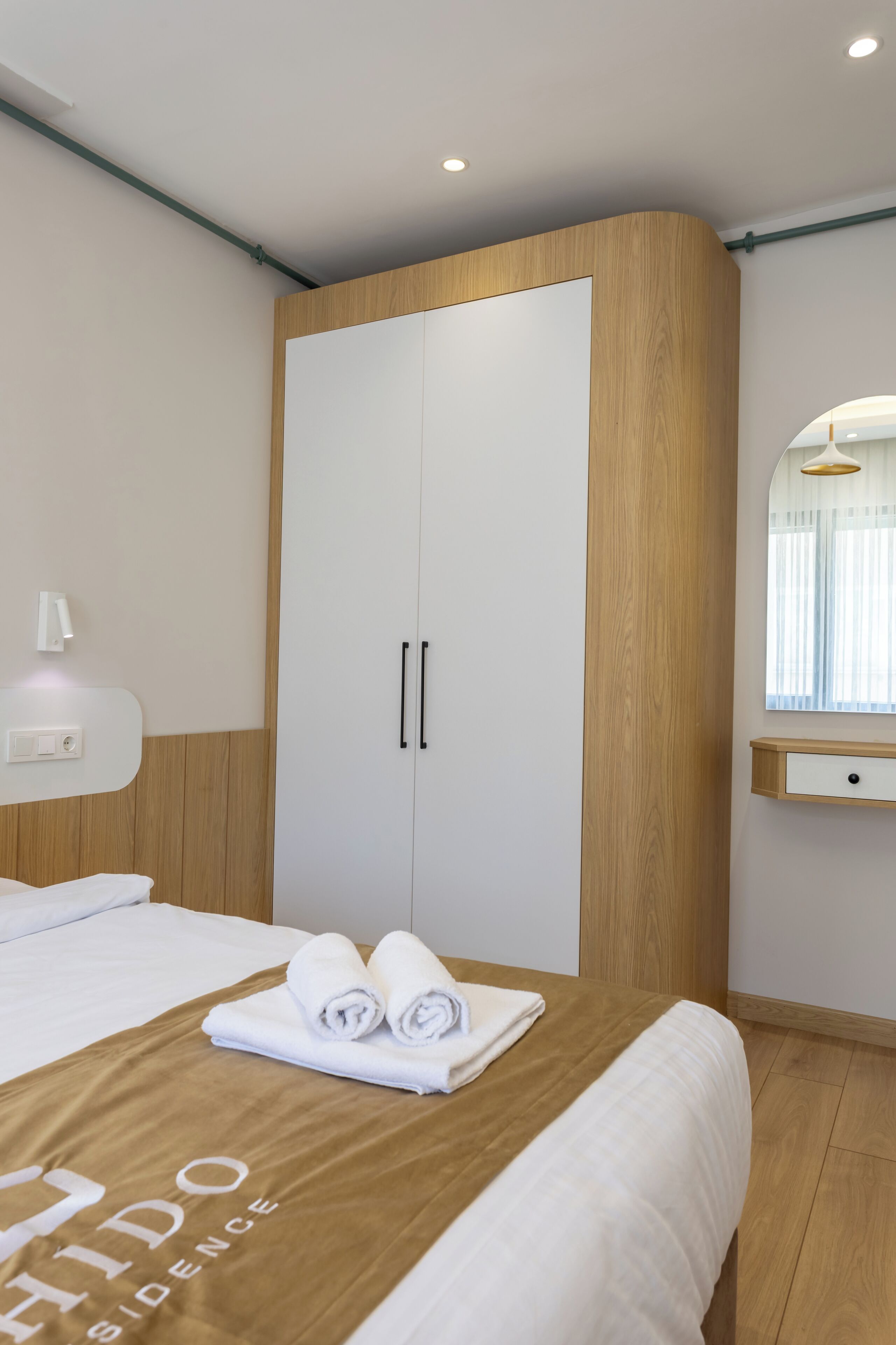 A hotel room with a bed, a wardrobe, a mirror, and a bedside table.