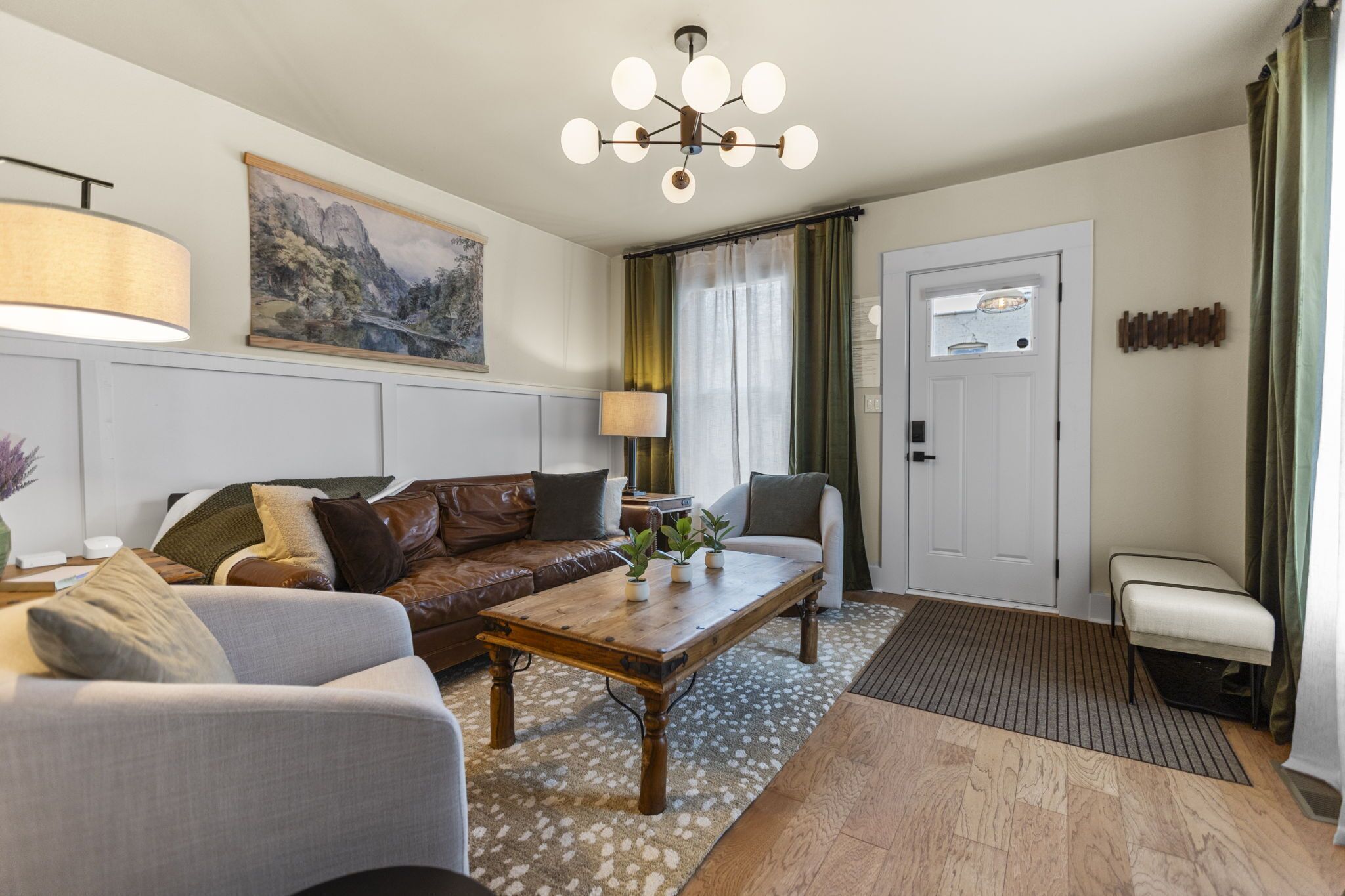 Un salon avec une table basse en bois, un canapé en cuir marron, un fauteuil blanc et un tableau accroché au mur.