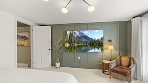 A bedroom with a bed, a TV mounted on the wall, a chair, and a small table. - Abode 81 in Newark (Newark)