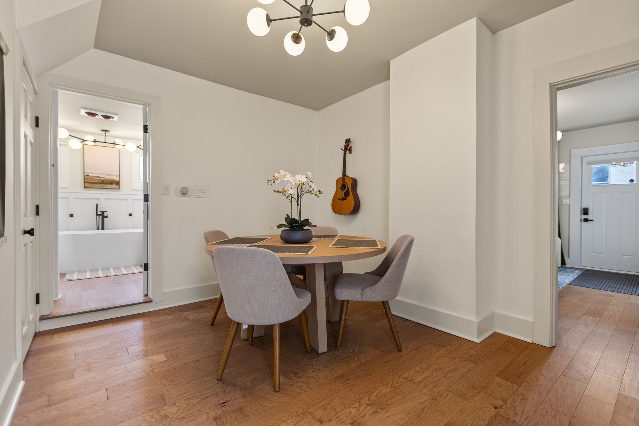 A dining area with a round table, four chairs, a guitar, and a vase of flowers.