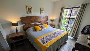 Un dormitorio con cabecera de madera, dos lámparas de noche, una cama con manta colorida y vistas al exterior a través de una ventana.