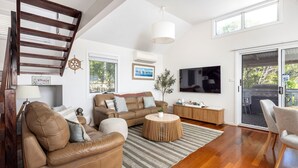 A spacious living room with a high ceiling, a wooden staircase, a large TV, and a sliding glass door leading to an outdoor area.