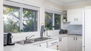A modern kitchen with white cabinetry, stainless steel appliances, and large windows offering views of trees.