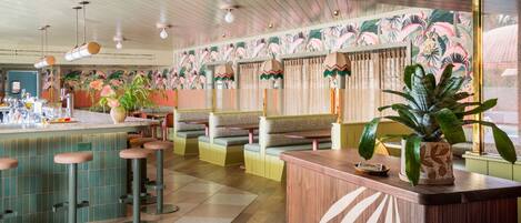 A restaurant interior with a bar area, seating with cushioned booths, and a tropical-themed wall.