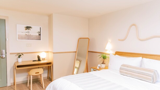 Une chambre d’hôtel comprenant un lit, un bureau avec une chaise, un miroir, une lampe et une plante.