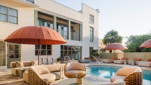 A poolside area with lounge chairs, a pool, and umbrellas. - Luxury Charleston Suite | Balcony + Spa Bath (Charleston)