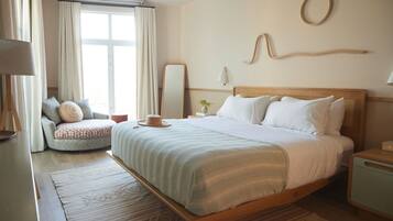 Une chambre à coucher avec un grand lit, une table de chevet, une commode, une chaise, un miroir et une fenêtre avec des rideaux.