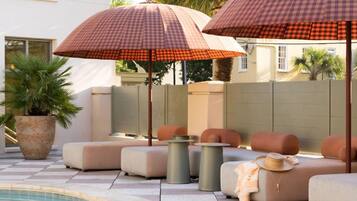 Un espace aménagé au bord de la piscine, avec des parasols à carreaux, des sièges rembourrés et une plante en pot.