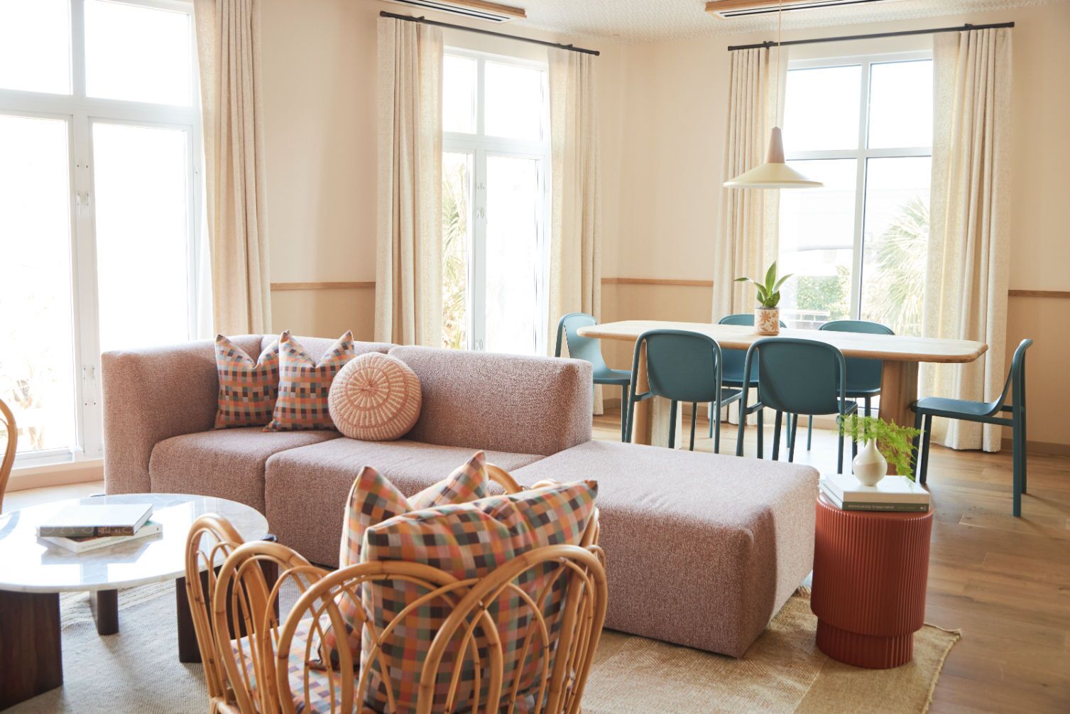 Een gezellige woonkamer met een bank, stoelen, een eettafel en grote ramen.