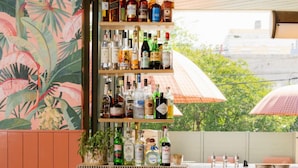 A bar area with a tropical mural, a variety of liquor bottles, and a view of greenery outside. - Luxury Charleston Suite | Balcony + Spa Bath (Charleston)