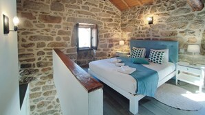 A stone-walled bedroom with a wooden ceiling, a bed with blue bedding, and a small window. - Aldeia de Pontes (Melgaco)