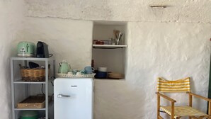 A compact room with a white fridge, a small shelf with kitchen items, a wicker basket, and a striped chair. - 5 km from the beaches of Pescoluse, charming trullo in the countryside in Salve (Salve)