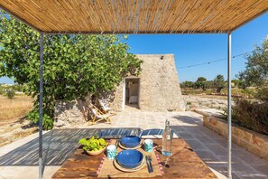 An outdoor dining area with a table set for two, a stone wall, and a view of the countryside.