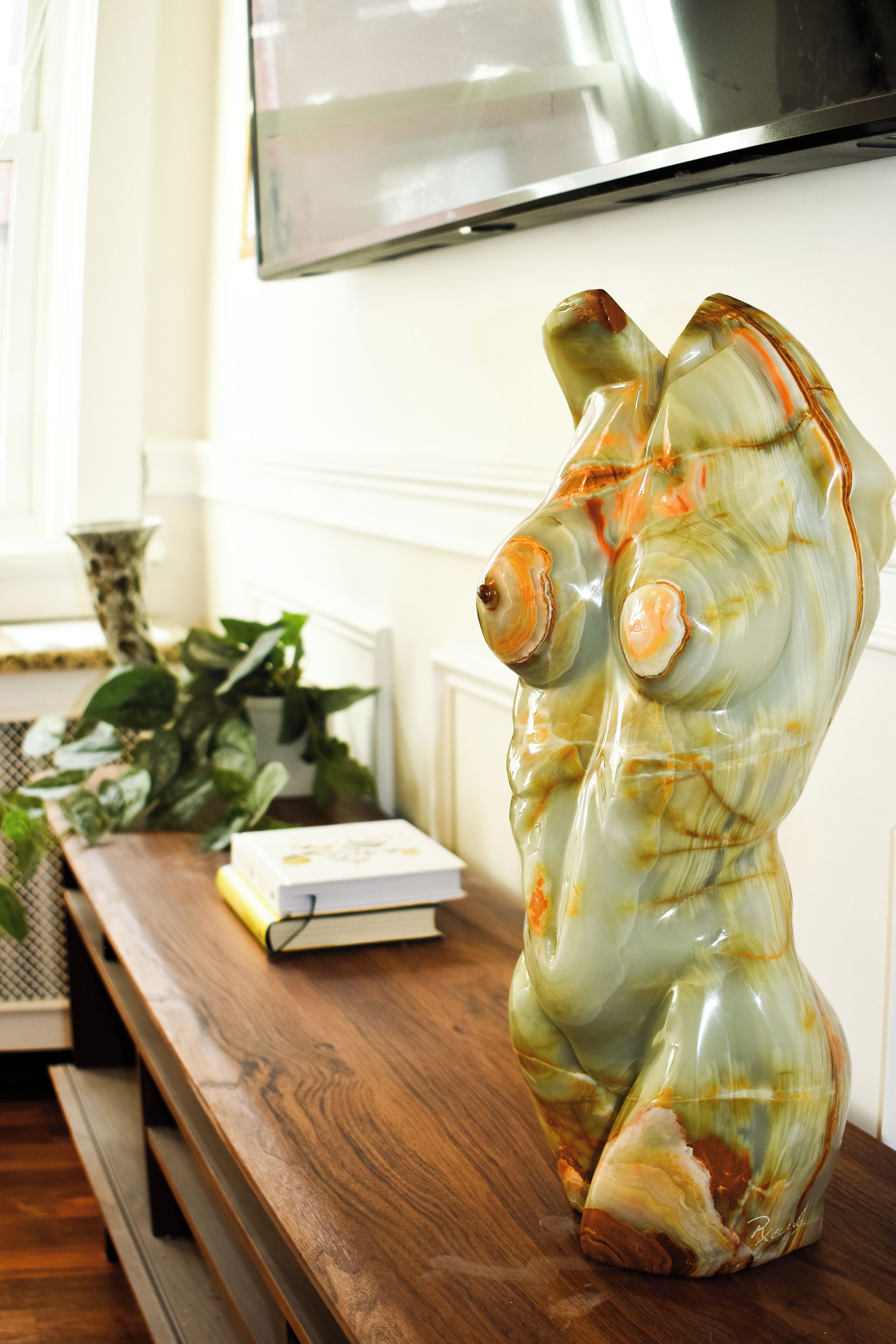A ceramic sculpture on a wooden table with a book and a potted plant in the background.
