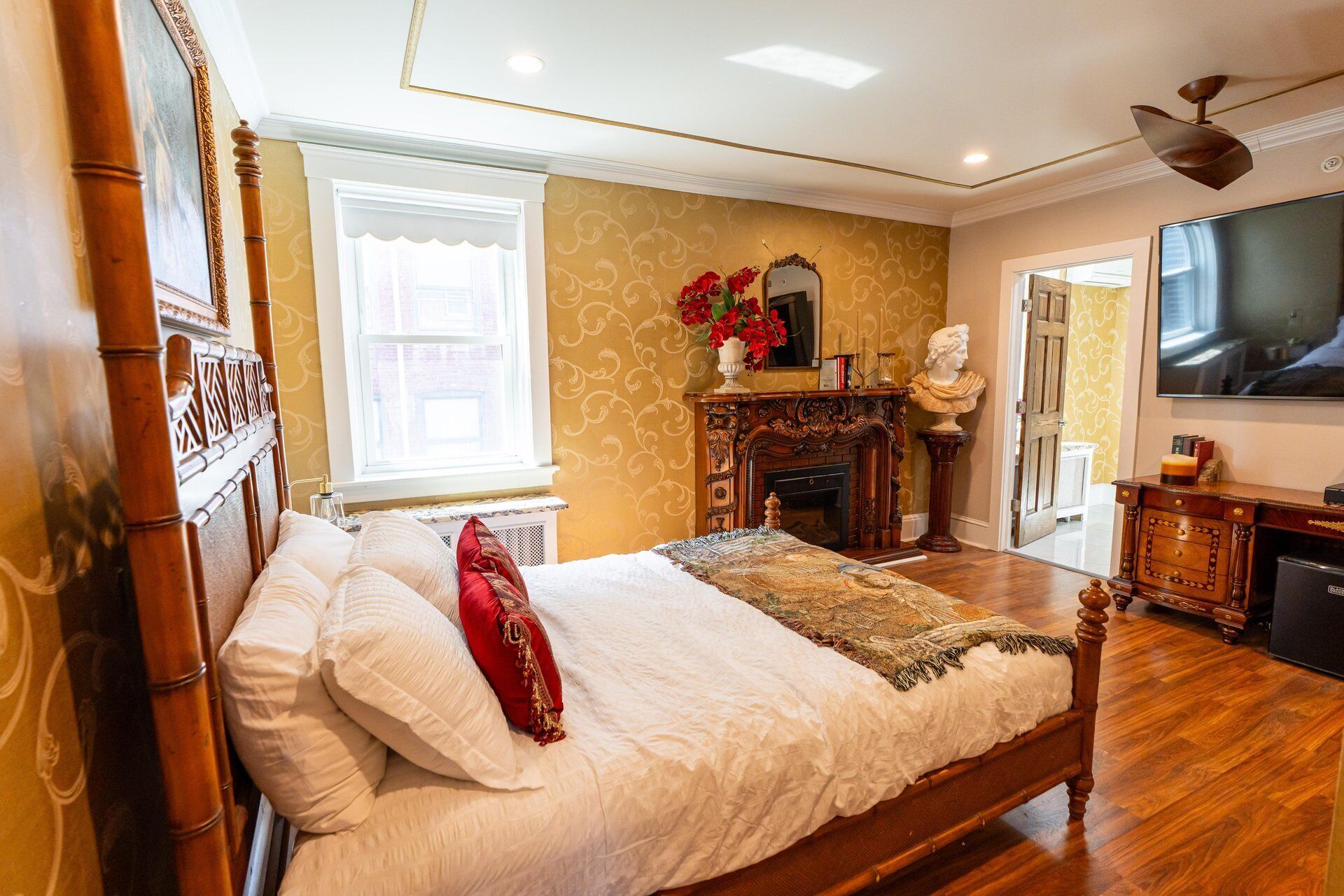 A bedroom with a large bed, a fireplace, a television, and a mirror.