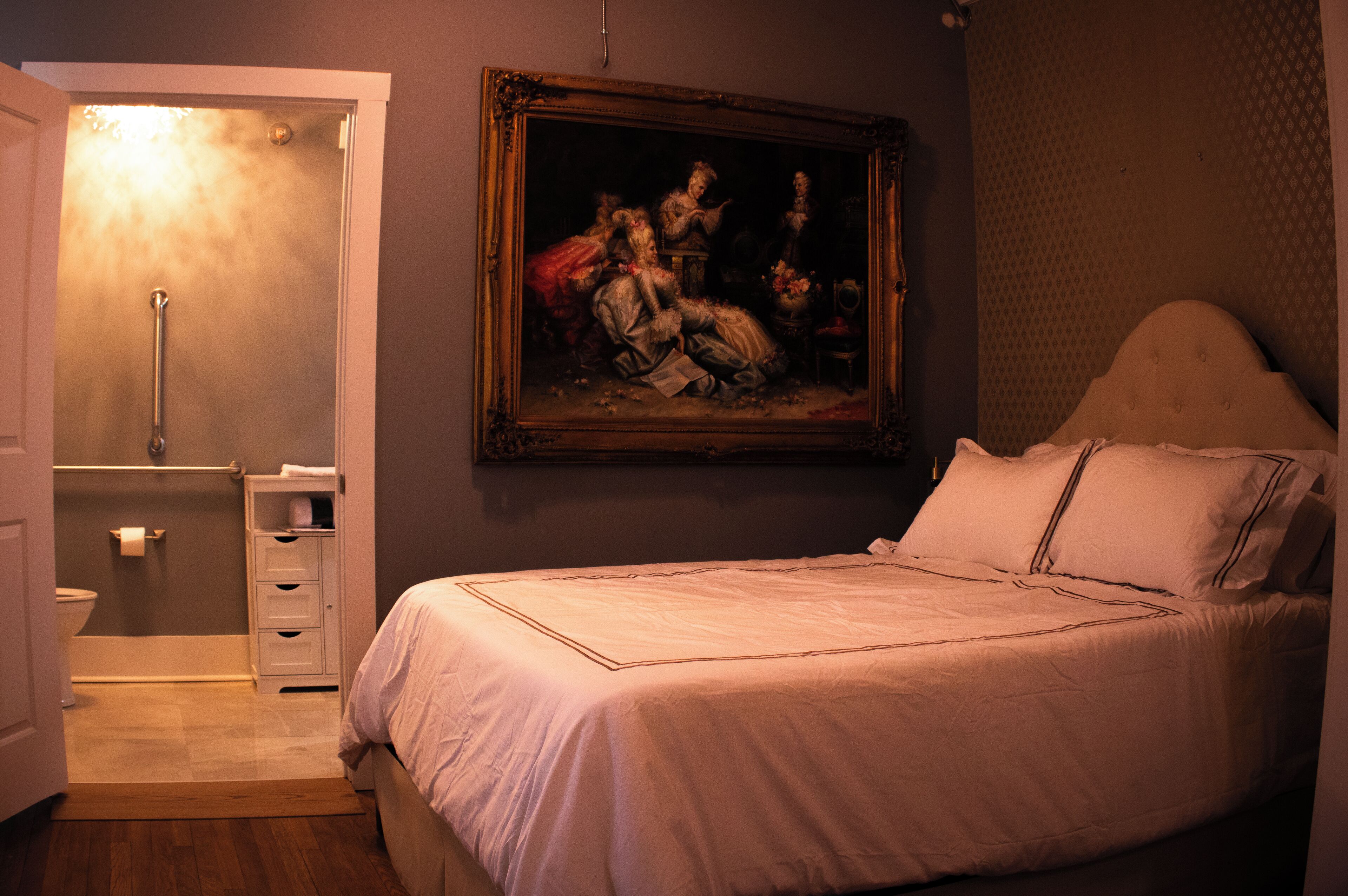 Un dormitorio con cama, un cuadro en la pared y un baño con inodoro y ducha.