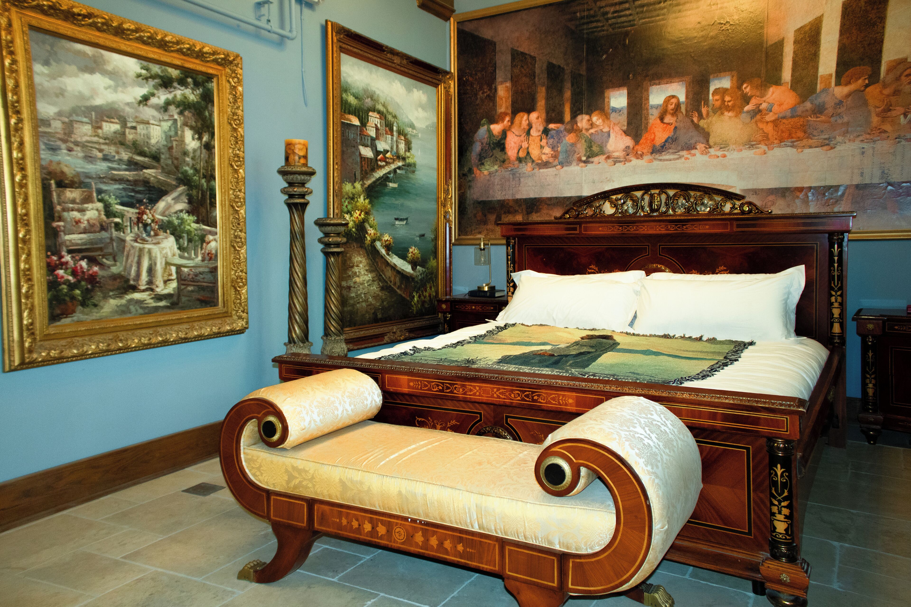 A large bed with a headboard, a bench, and a painting of a river scene.
