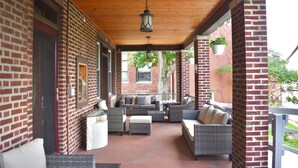 Een overdekt terras met rieten meubilair, een hanglamp en bakstenen muren.