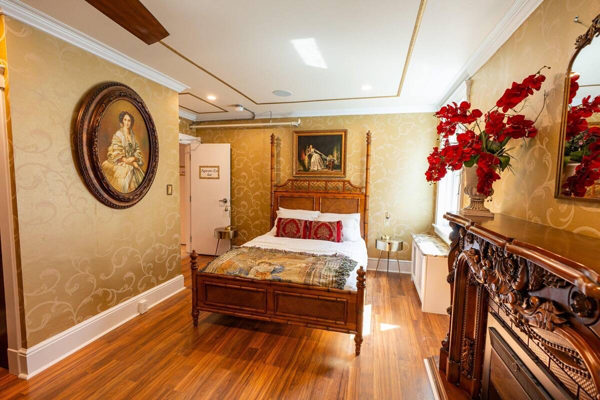 Une chambre spacieuse avec un grand lit, une commode en bois, un miroir et une porte portant l’inscription « Entrée de la réception ».