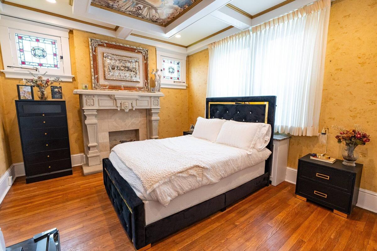 Une chambre à coucher avec un grand lit, une cheminée, une table de chevet et une commode.