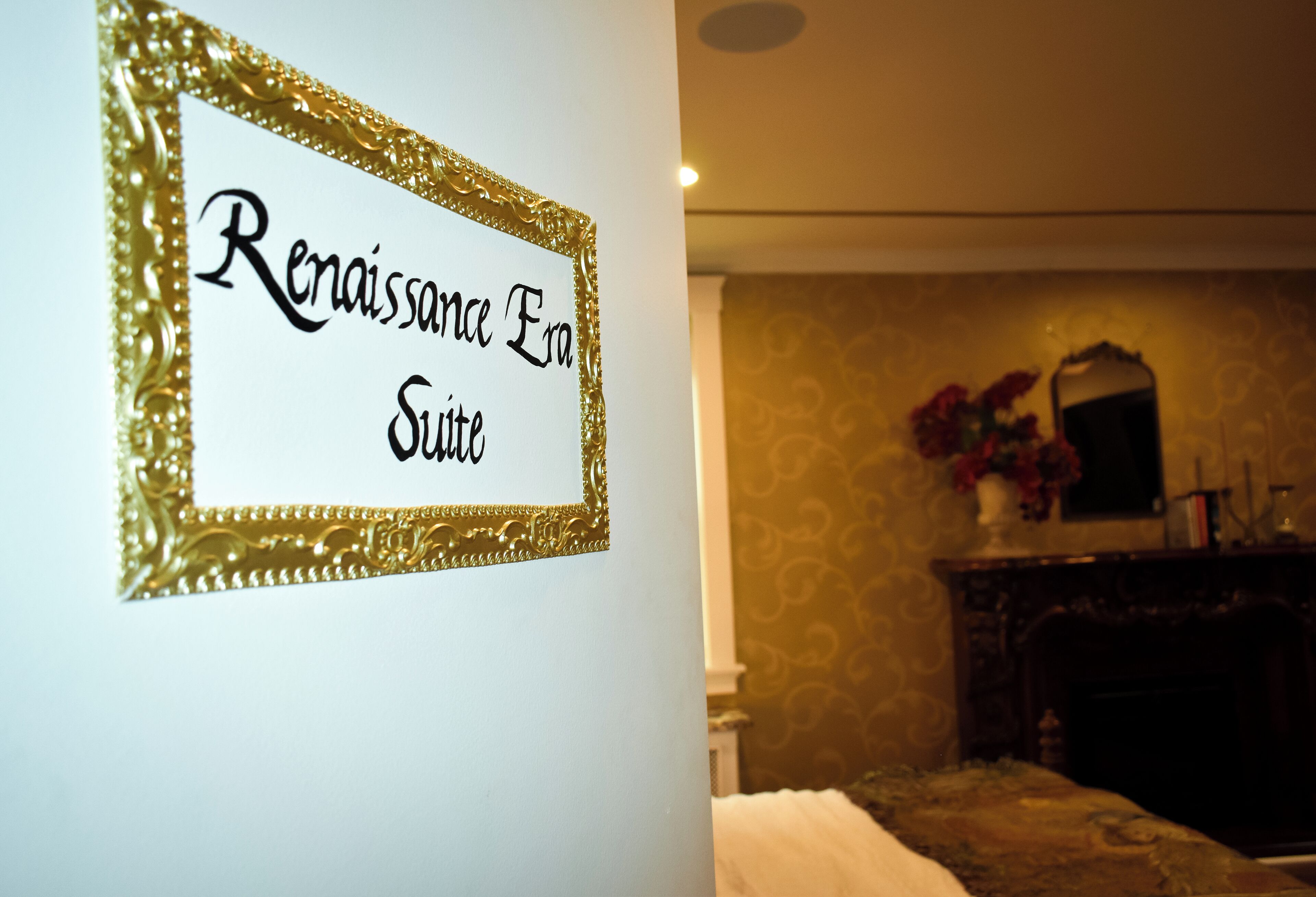 A sign reading "Renaissance Era Suite" in a room with a patterned wallpaper and a fireplace.