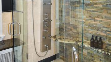 A glass-enclosed shower with a stone wall and a marble countertop.