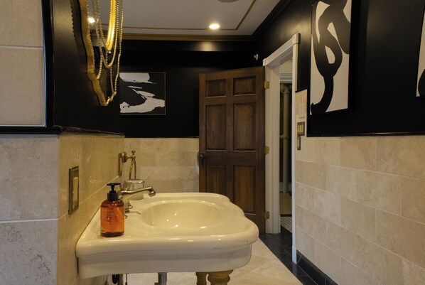A bathroom with a white sink, gold faucets, and a bottle of soap. There is a door and a wall with a black and white abstract design. - Chateau Connellsville (Connellsville)