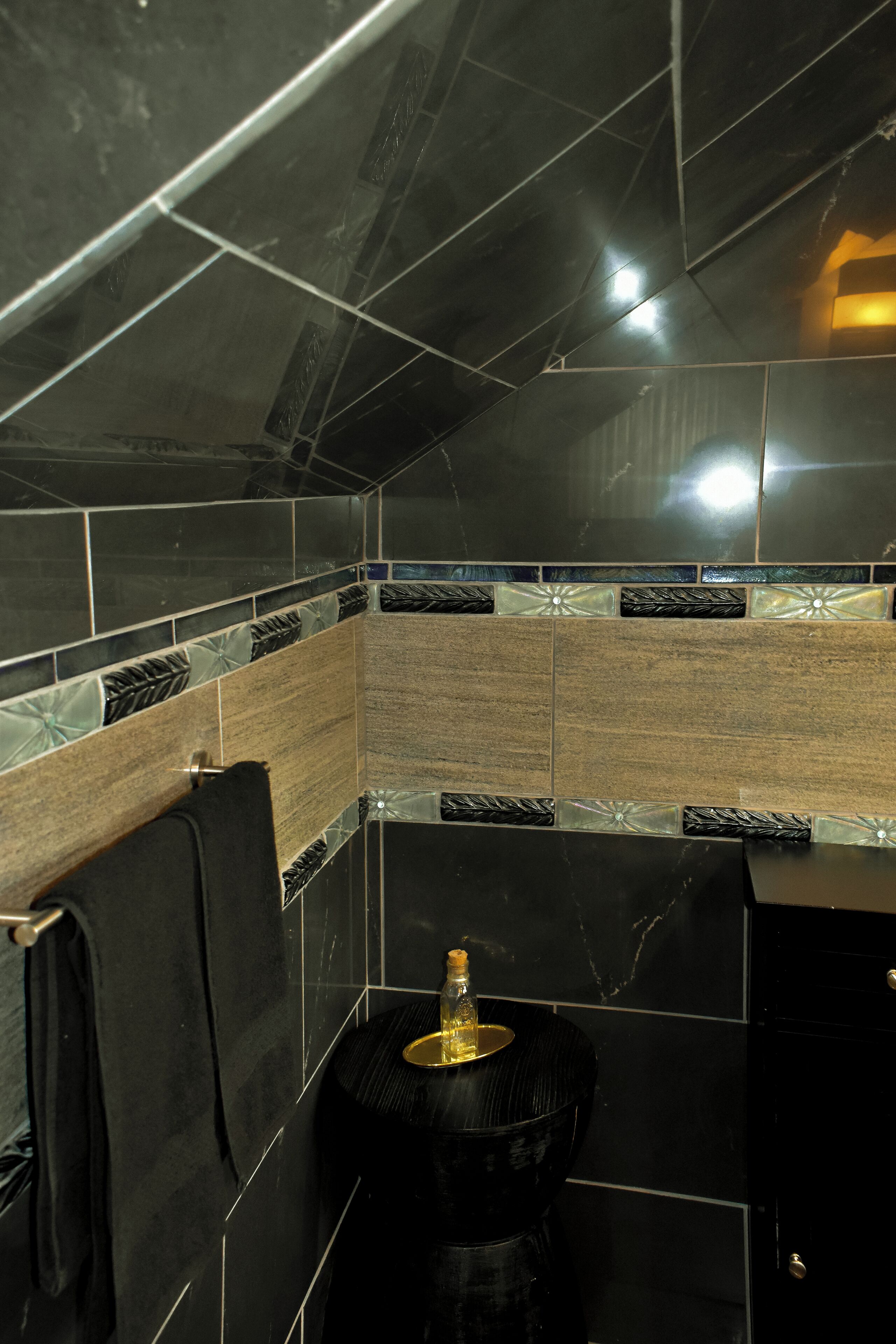 Un bagno con piastrelle nere e marroni, un porta asciugamani e un water con base dorata.