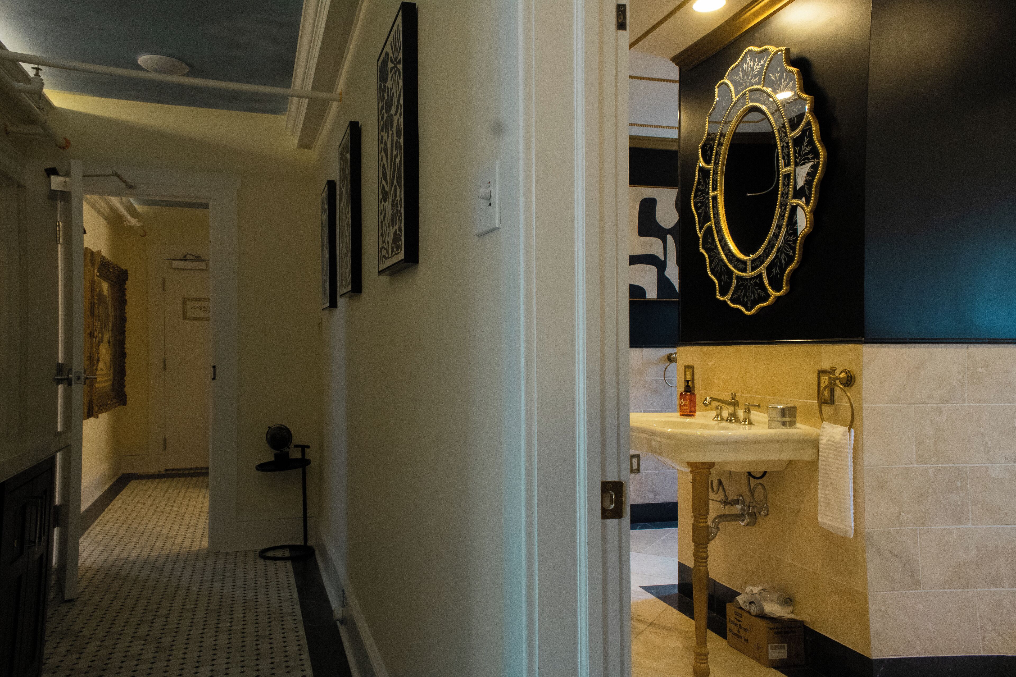Um corredor com piso estampado, uma porta que dá para um banheiro e um espelho fixado na parede.