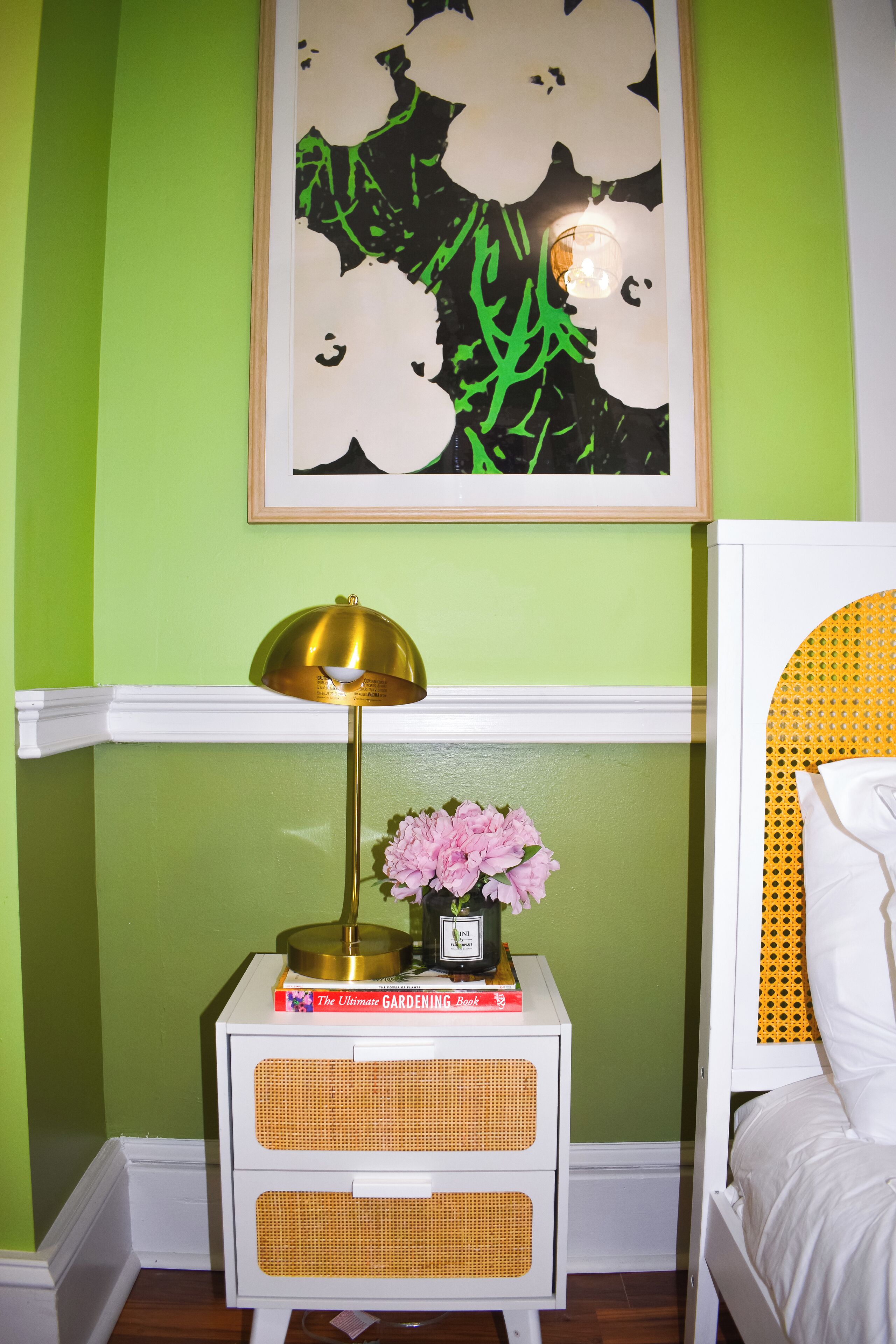 Una camera da letto con una parete verde, un comodino bianco con una lampada, un quadro incorniciato e un letto con una testiera gialla.
