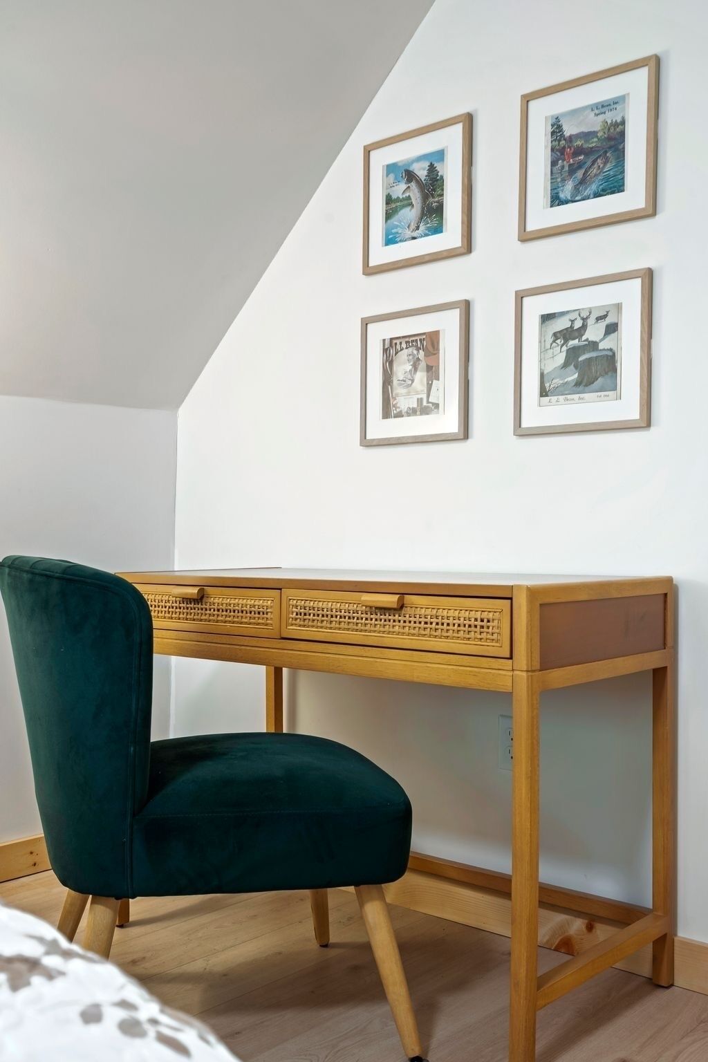 A room with a wooden desk, a green chair, and four framed pictures on the wall.