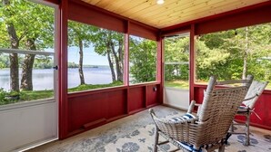 A covered porch with a view of a lake and trees, featuring two wicker chairs and a patterned rug. - Salt water hot tub, king size beds, dog friendly, lake front, dock, boat launch (Canaan)