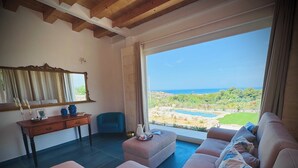 Ein Wohnzimmer mit einer Couch, einem Tisch und einem Stuhl. Blick auf einen Pool und Grünflächen.