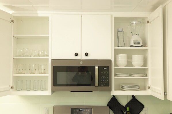 A kitchen with white cabinets, a microwave, a blender, and glassware.