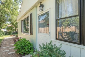 A house with a front door, two windows with shutters, a small porch, and a wooden fence in the background.