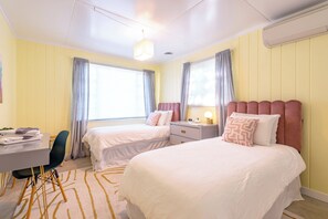A hotel room with two beds, a desk, a chair, and a window with curtains.