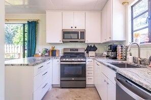 A modern kitchen with white cabinetry, a stainless steel stove, a microwave, and a sink.