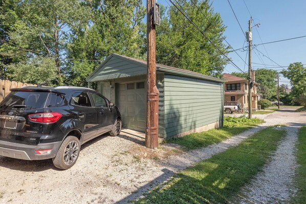 A black SUV parked next to a small shed with a gravel driveway leading to a house.
