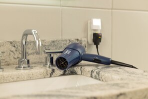 A hair dryer on a bathroom countertop near a sink and faucet.