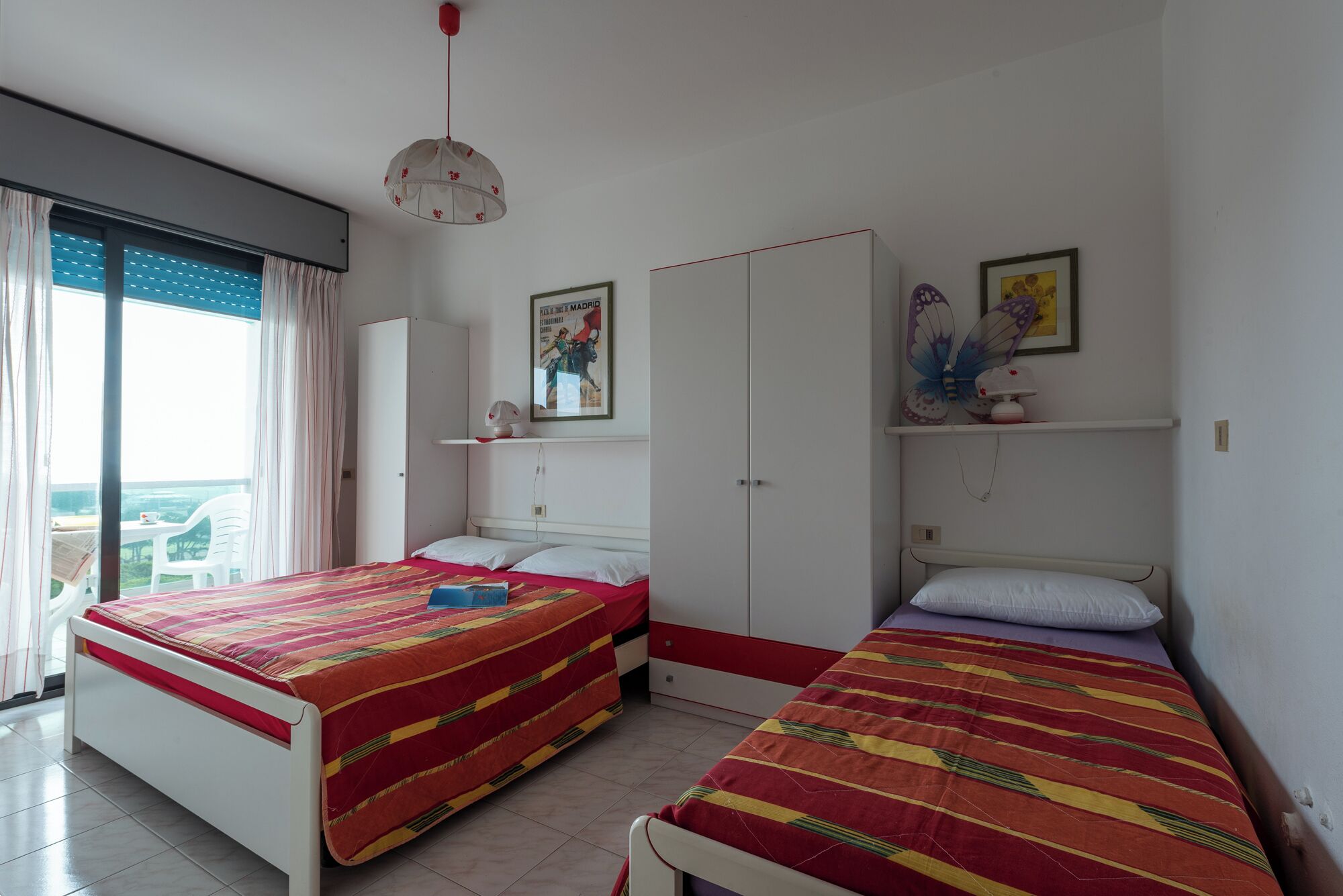 A bedroom with two beds, a wardrobe, a ceiling fan, and a window with curtains.