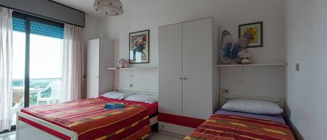 A bedroom with two beds, a wardrobe, a ceiling fan, and a window with curtains.